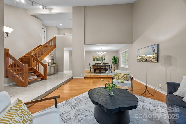 living room featuring stairs, an inviting chandelier, wood finished floors, and a towering ceiling