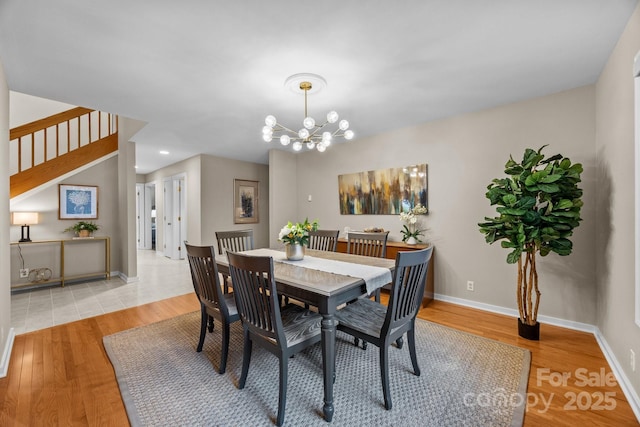 dining space featuring baseboards, an inviting chandelier, wood finished floors, and stairway