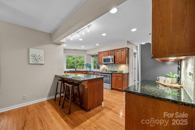 kitchen featuring brown cabinetry, a kitchen bar, light wood-style flooring, appliances with stainless steel finishes, and backsplash