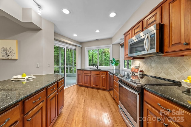 kitchen featuring dark stone counters, light wood finished floors, brown cabinets, and stainless steel appliances