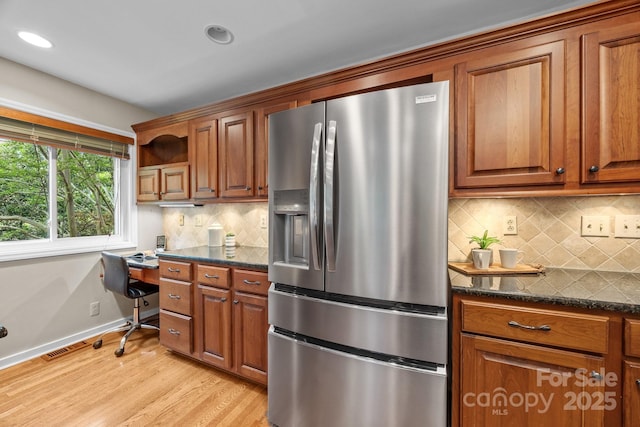 kitchen with brown cabinetry, stainless steel refrigerator with ice dispenser, recessed lighting, built in desk, and light wood finished floors
