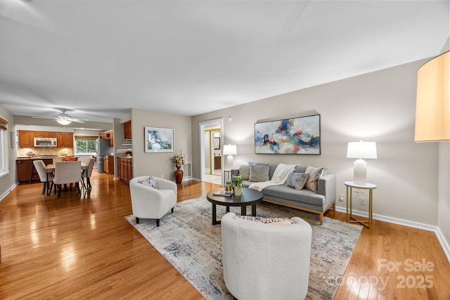 living room with light wood-style floors, baseboards, and ceiling fan