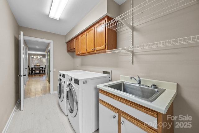 laundry area with washing machine and dryer, baseboards, light wood-type flooring, a sink, and cabinet space