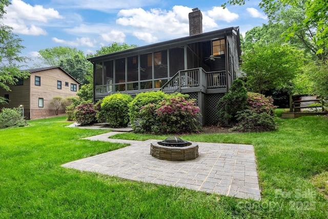 rear view of house with an outdoor fire pit, a sunroom, a chimney, a patio area, and a lawn