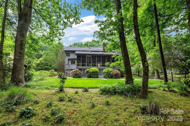 back of property featuring a lawn, fence, a chimney, and a sunroom