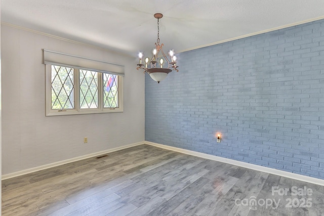 empty room with a notable chandelier, baseboards, brick wall, crown molding, and wood finished floors