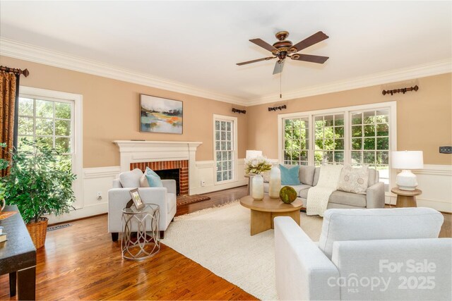 1233 Weymouth Ln, Charlotte, NC 28270 - living room with crown molding, wood finished floors, a fireplace, ceiling fan, and a wainscoted wall