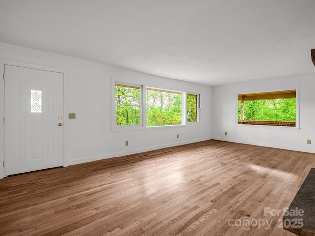 unfurnished living room featuring healthy amount of natural light, wood finished floors, and baseboards