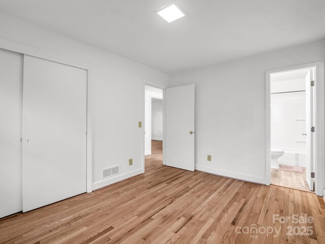 unfurnished bedroom featuring light wood-style floors, ensuite bathroom, a closet, and baseboards