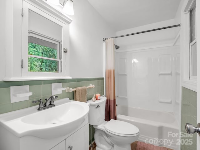 bathroom with tile walls, toilet, shower / bath combination with curtain, vanity, and wainscoting