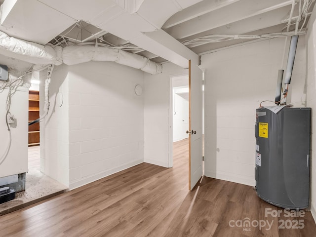 unfinished basement featuring electric water heater, wood finished floors, and concrete block wall
