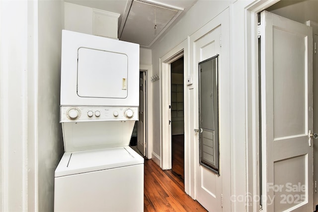 clothes washing area featuring stacked washer / dryer, laundry area, wood finished floors, baseboards, and attic access