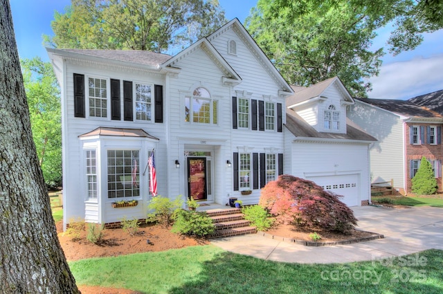 colonial inspired home with an attached garage, driveway, and roof with shingles