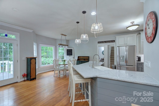 kitchen with light stone counters, a sink, stainless steel fridge with ice dispenser, and light wood-style floors