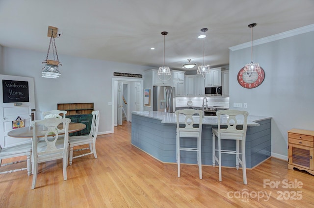 kitchen featuring appliances with stainless steel finishes, hanging light fixtures, a peninsula, decorative backsplash, and light wood-type flooring
