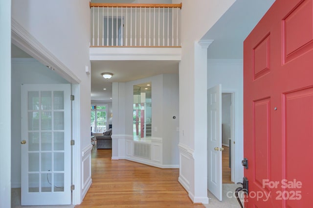 foyer featuring visible vents, ornamental molding, a towering ceiling, a decorative wall, and light wood-type flooring
