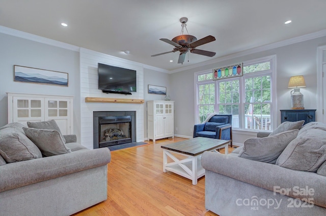 living area with crown molding, a large fireplace, recessed lighting, and light wood-style flooring