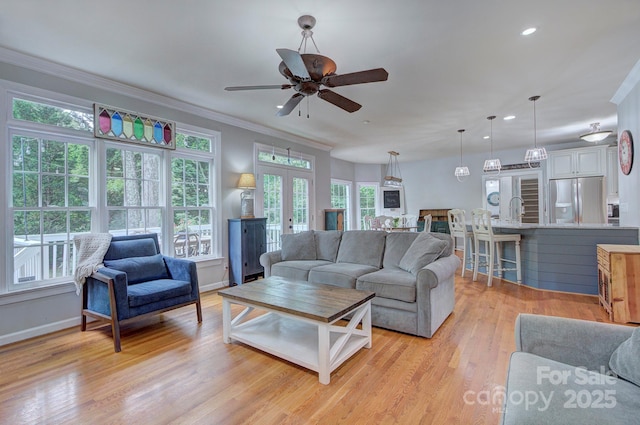 living area featuring crown molding, baseboards, french doors, and a healthy amount of sunlight