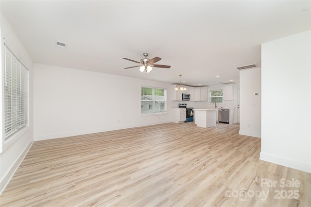 unfurnished living room with visible vents, baseboards, light wood finished floors, and ceiling fan with notable chandelier