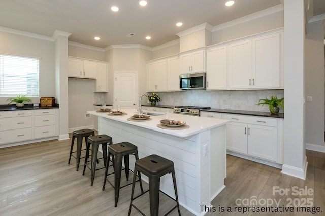 kitchen featuring a sink, appliances with stainless steel finishes, a kitchen breakfast bar, white cabinetry, and decorative backsplash