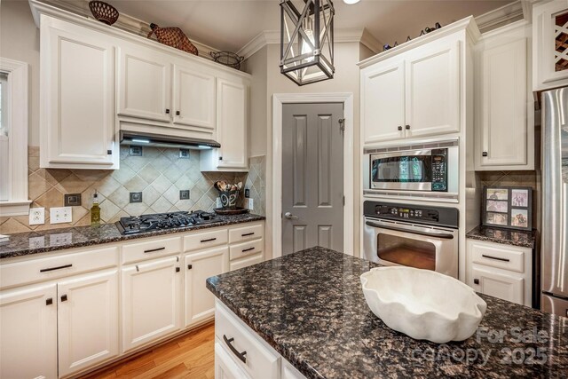 19729 Callaway Hills Ln, Davidson, NC 28036 - kitchen with under cabinet range hood, tasteful backsplash, dark stone counters, and stainless steel appliances
