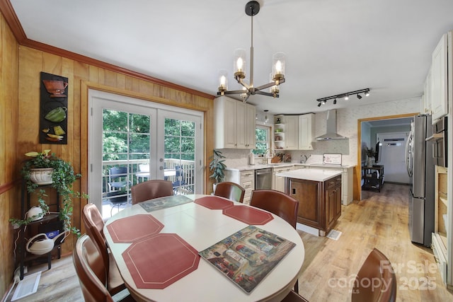 dining space with a notable chandelier, light wood finished floors, rail lighting, french doors, and wallpapered walls