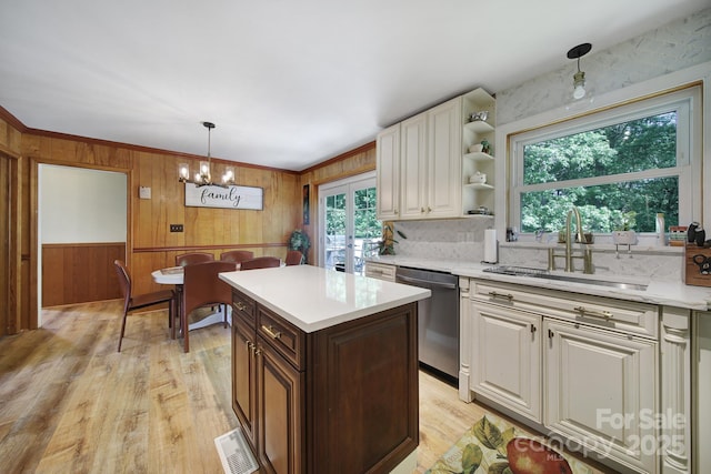 kitchen with visible vents, dishwasher, a sink, light countertops, and wooden walls