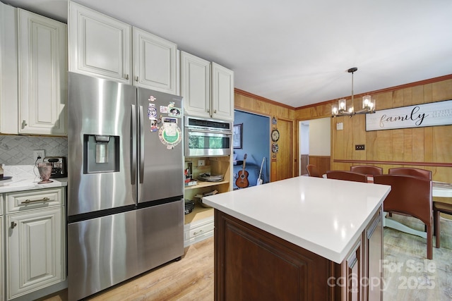 kitchen featuring an inviting chandelier, wood walls, light countertops, light wood finished floors, and stainless steel appliances