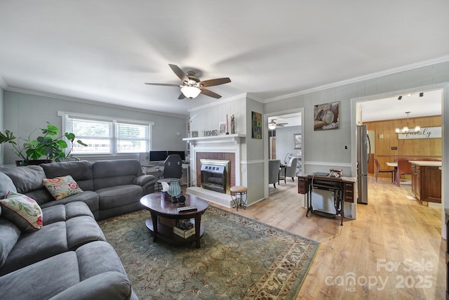 living room featuring a fireplace, ornamental molding, ceiling fan with notable chandelier, and light wood-style floors