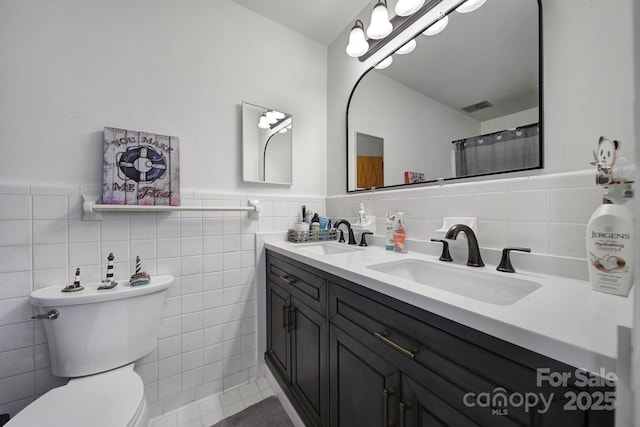 full bathroom with tile walls, toilet, visible vents, and a sink