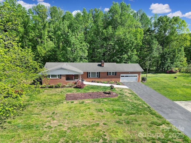 single story home featuring a garage, a front lawn, a chimney, brick siding, and driveway