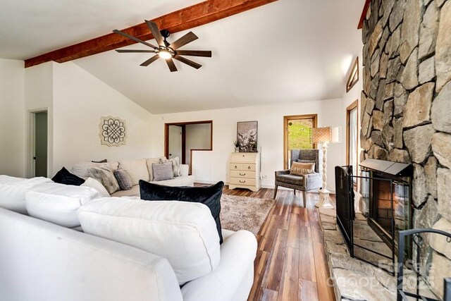 living room with ceiling fan, lofted ceiling with beams, a stone fireplace, and hardwood / wood-style floors