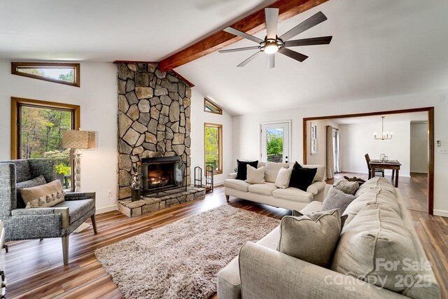 living area with a stone fireplace, wood finished floors, baseboards, lofted ceiling with beams, and ceiling fan with notable chandelier