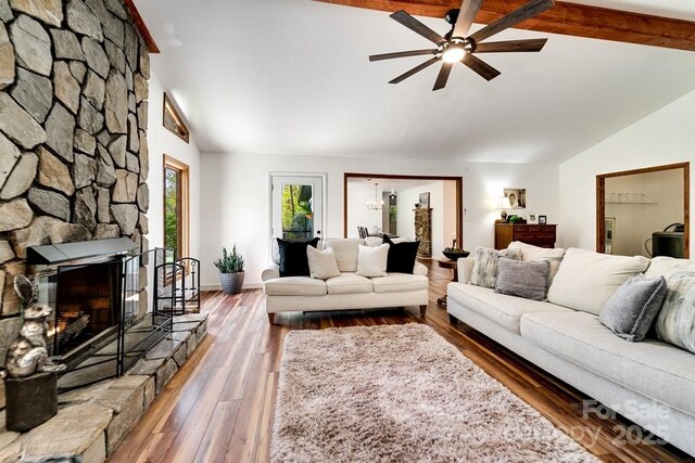 living room featuring a stone fireplace, lofted ceiling with beams, ceiling fan, and wood finished floors