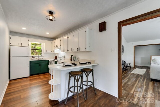 kitchen featuring white appliances, a peninsula, white cabinetry, and a sink