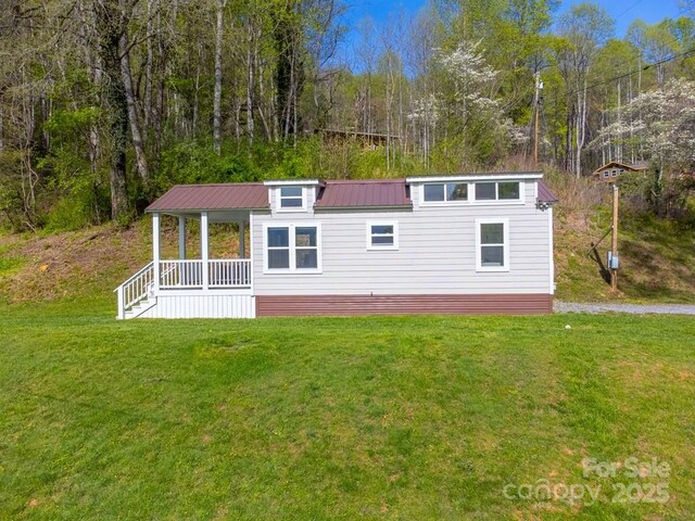 view of front facade featuring covered porch, a wooded view, metal roof, and a front yard