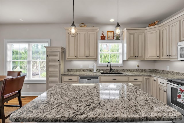 kitchen with a center island, a sink, cream cabinets, appliances with stainless steel finishes, and light stone countertops