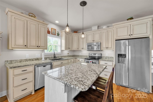kitchen featuring a kitchen breakfast bar, a sink, light wood-type flooring, cream cabinets, and appliances with stainless steel finishes