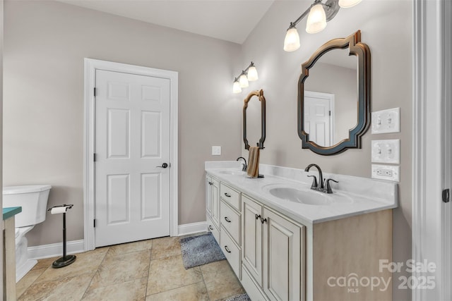 full bath with baseboards, a sink, double vanity, and toilet