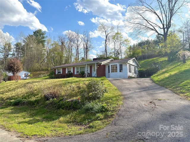 ranch-style house featuring covered porch, driveway, a chimney, and a front lawn