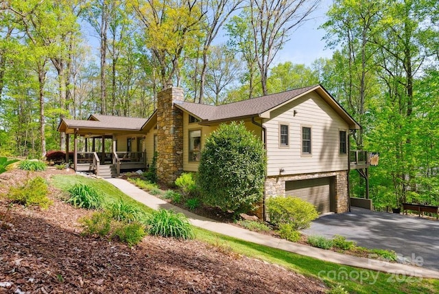 view of front of home featuring a chimney, covered porch, aphalt driveway, a garage, and stone siding