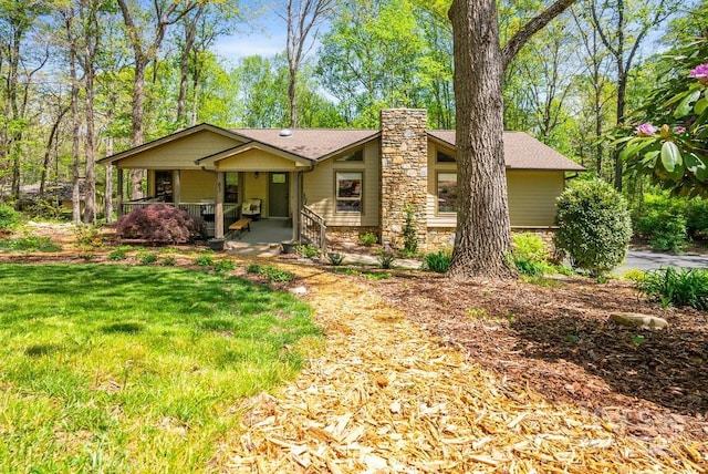 view of front facade with a front yard, covered porch, and a chimney