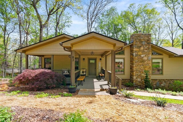 view of front of house featuring stone siding, covered porch, and a chimney