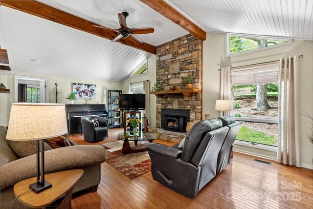 living room featuring wood-type flooring, vaulted ceiling with beams, a ceiling fan, visible vents, and a stone fireplace