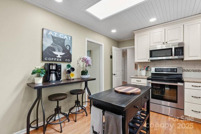 kitchen featuring recessed lighting, light wood-style flooring, decorative backsplash, stainless steel appliances, and white cabinets