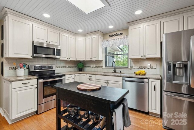 kitchen with light wood finished floors, a sink, stainless steel appliances, decorative backsplash, and white cabinetry