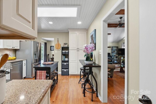 kitchen with light stone counters, white cabinetry, ceiling fan, stainless steel appliances, and light wood finished floors