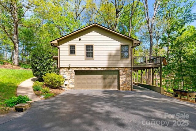 view of side of home featuring a garage, aphalt driveway, a wooden deck, and stone siding