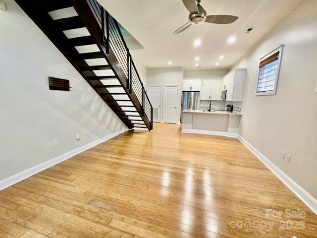 unfurnished living room with recessed lighting, baseboards, light wood-style flooring, stairs, and ceiling fan