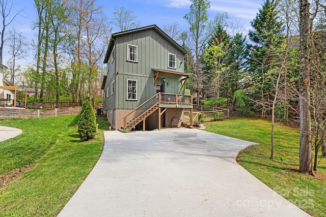 view of front facade with stairway, concrete driveway, board and batten siding, a front yard, and a wooden deck